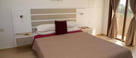 A bedroom with a large bed, a nightstand, a drawer, a dreamcatcher on the wall, and a window with curtains.