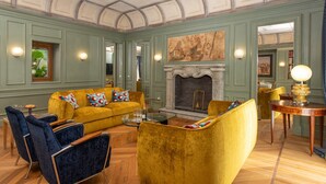 A room with a yellow sofa, blue armchairs, a fireplace, and a dining area with a glass table. - Belvedere Guastella A 8 Emma Villas (Noto)