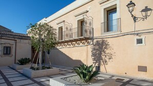 A courtyard with a tree, a small garden, and a building with balconies and windows. - Belvedere Guastella B 4 Emma Villas (Noto)