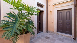 A courtyard with a large potted plant, a door, and a tiled floor. - Belvedere Guastella B 4 Emma Villas (Noto)