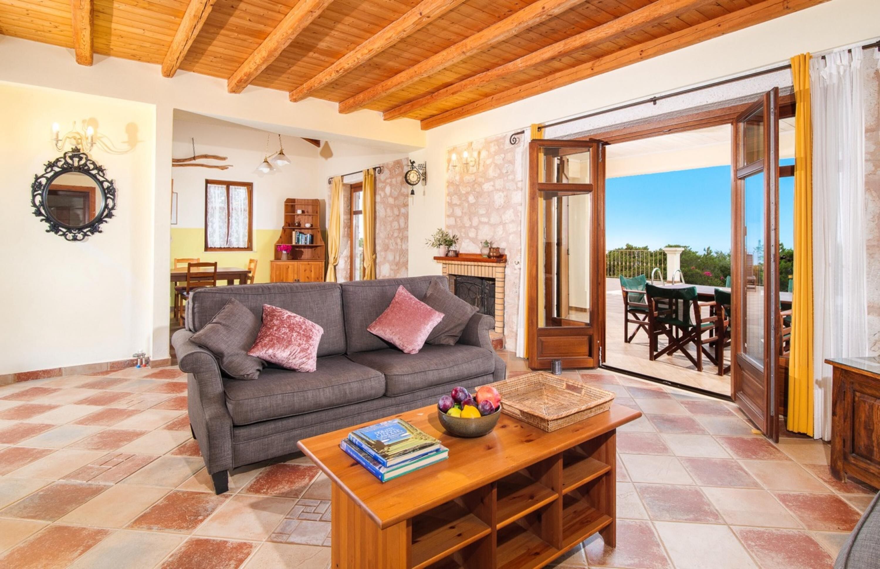A cozy living room with a sofa, a coffee table with books and fruit, and a view of the outdoor patio.