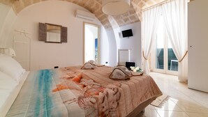 A bedroom with a large bed, a flat-screen TV, a window with curtains, and a stone ceiling. - Gioia Casa Vacanze in Monopoli (Monopoli)