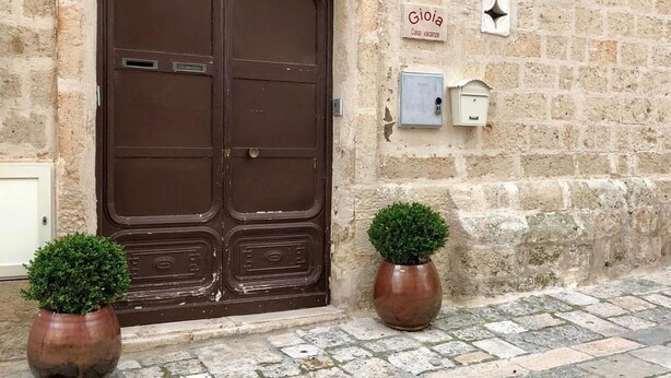 A stone building with a large brown double door, two potted plants, and a sign indicating 'Gioia Casa vacanze'. - Gioia Casa Vacanze in Monopoli (Monopoli)
