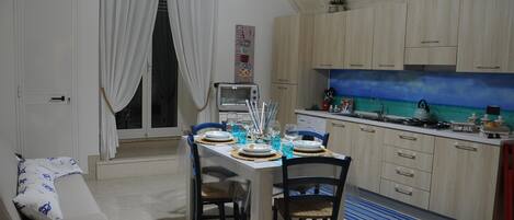 Cuina compacta amb zona de dinar, forn encastrat i una finestra petita amb cortines.