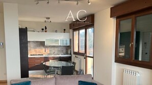 Een moderne woonkamer met een grijze bank, een eettafel en een keuken op de achtergrond.