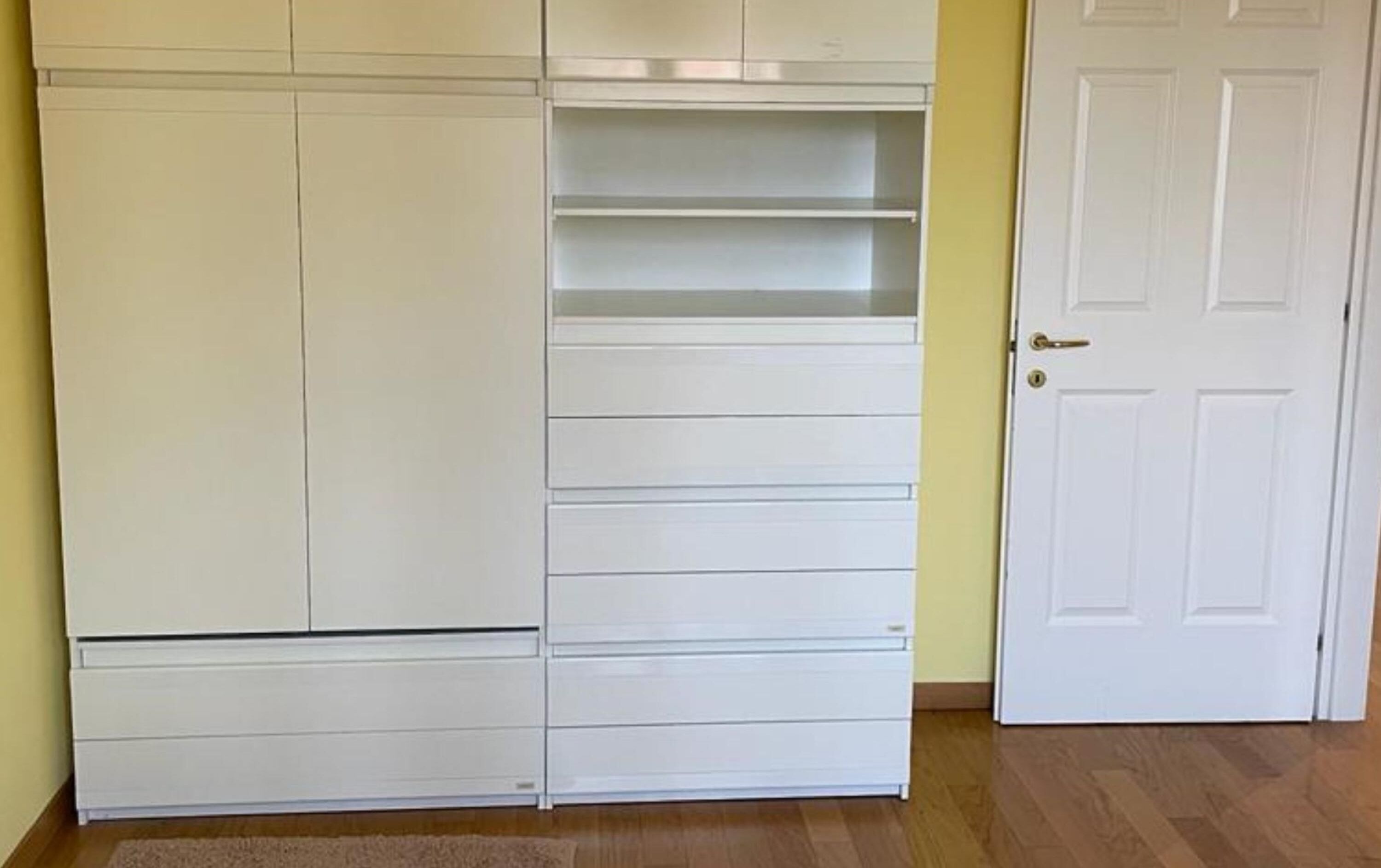 Ein weißer Kleiderschrank mit mehreren Schubladen und Regalen, ein Holzboden und eine weiße Tür.