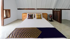Habitación de hotel con cama, dos almohadas de diseños geométricos, un ventilador y una ventana con cortinas.