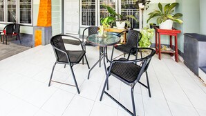 A patio area with a round table and four chairs, surrounded by potted plants and a red table.