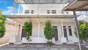 Un edificio de dos pisos con techo plano, un porche cubierto y un pequeño jardín con tres árboles.