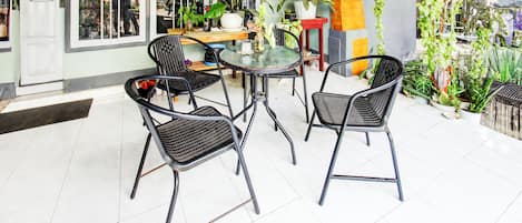 A patio area with a round table and four chairs, surrounded by potted plants and a tiled floor.