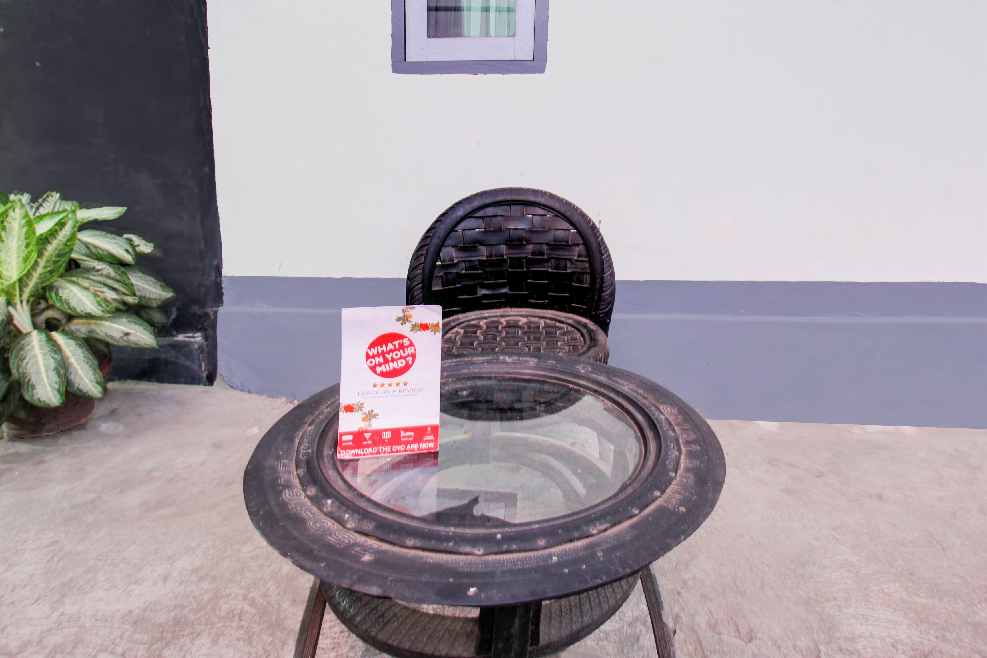 A round glass table with a black woven chair, a potted plant, and a sign on the table.