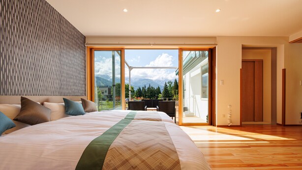 A modern bedroom with a large bed, a view of mountains, and a balcony with outdoor furniture. - Gram Cottage Hakuba (Hakuba)