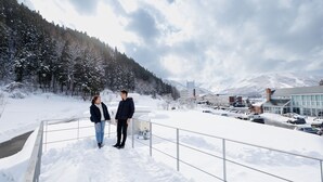 A snowy landscape with a building and parked cars. - Gram Cottage Hakuba (Hakuba)