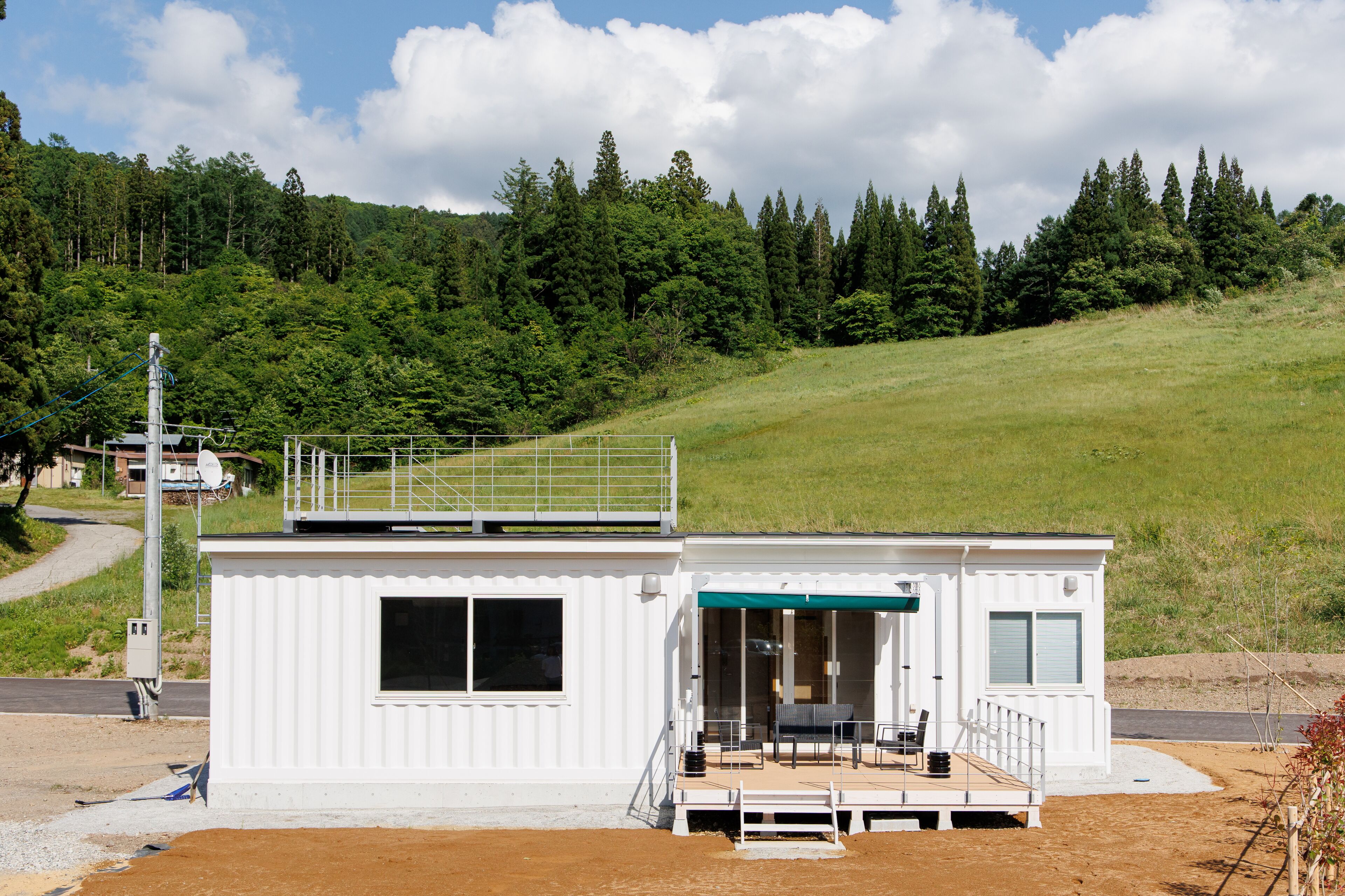 A white cabin with a deck, large windows, and a green awning.