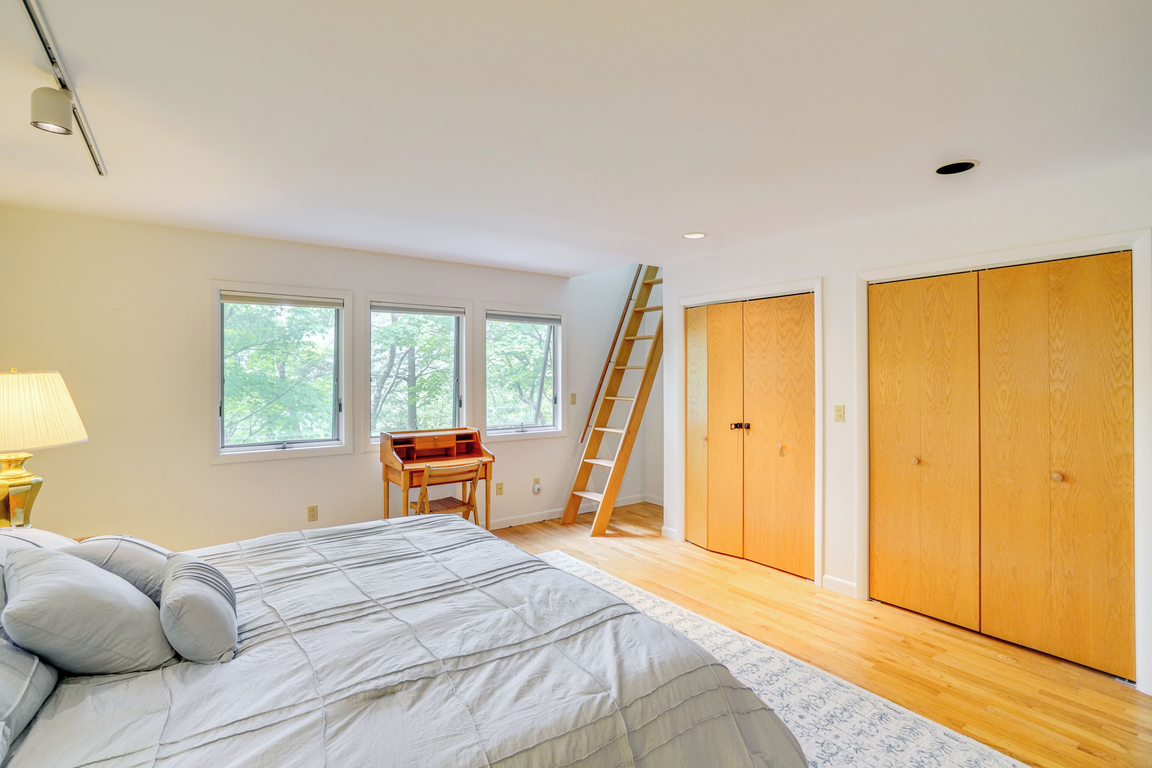A bedroom with a bed, a desk, a ladder, and a wardrobe.