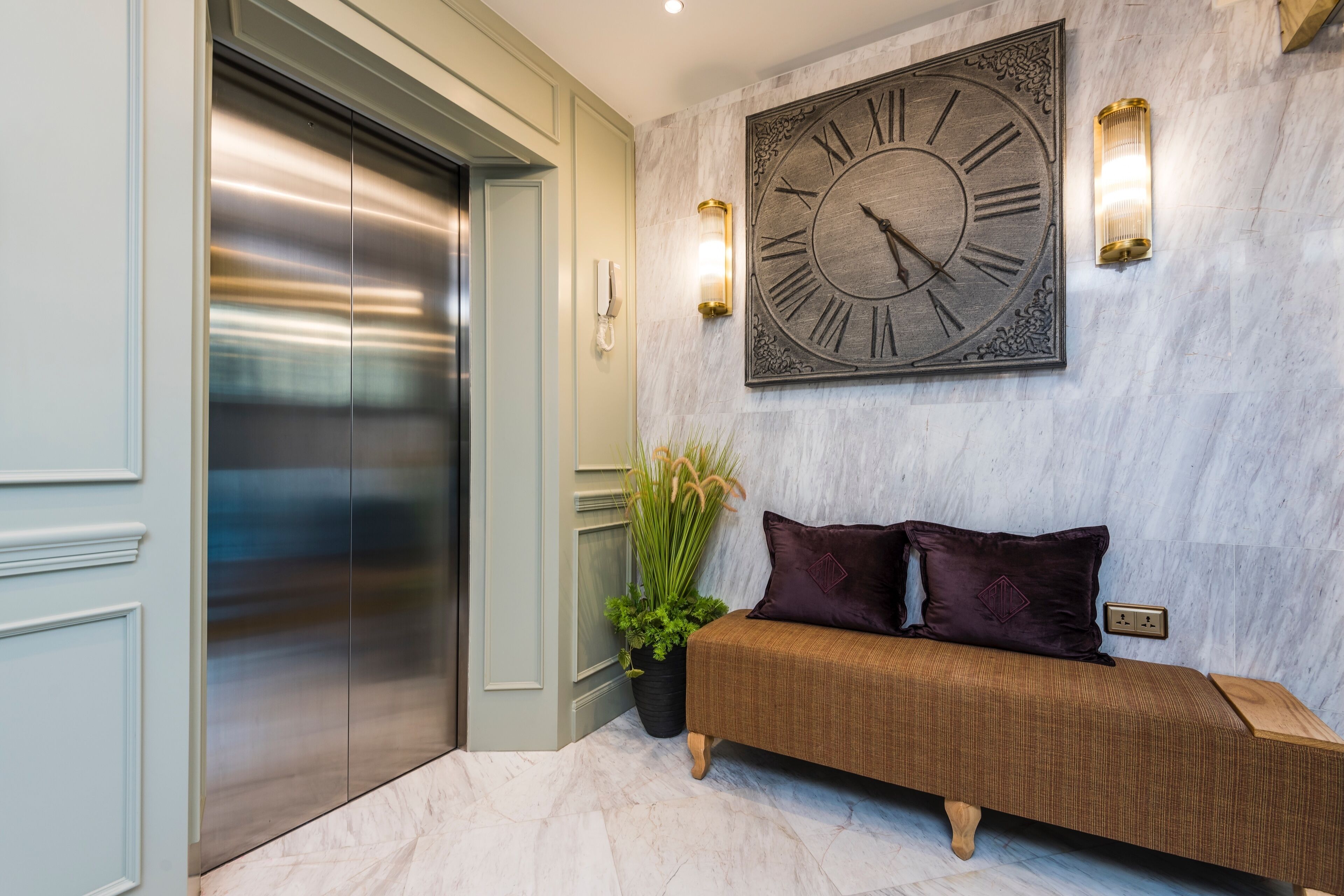 A lobby with a marble floor, a large wall clock, a bench, and an elevator.