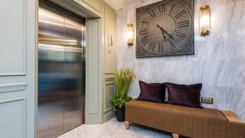 A lobby with a marble floor, a large wall clock, a bench, and an elevator.
