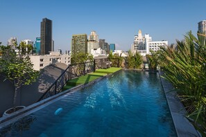 A swimming pool with a cityscape view, surrounded by greenery and modern buildings.