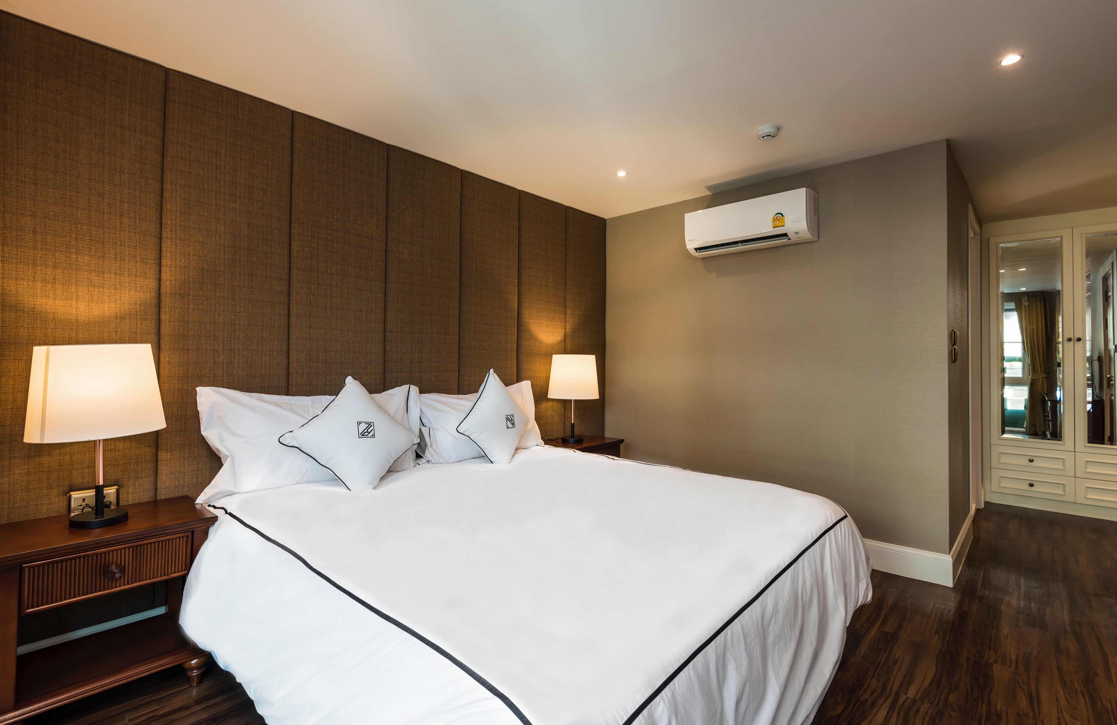 A hotel room with a large bed, two bedside lamps, an air conditioning unit, and a wardrobe.