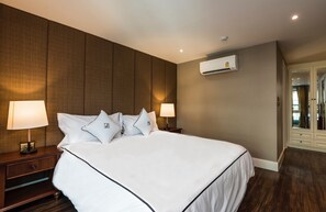 A hotel room with a large bed, two bedside lamps, an air conditioning unit, and a wardrobe.