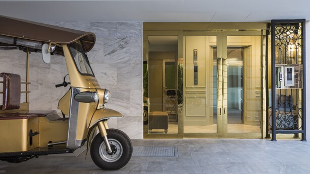 Uma scooter antiga estacionada em ambiente interno, entrada por porta de vidro e um elevador moderno.