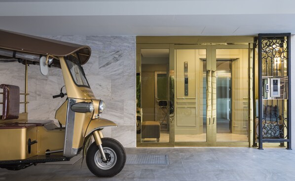 A vintage scooter parked indoors, a glass door entrance, and a modern elevator.