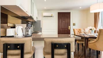 A modern hotel room with a dining area, kitchenette, and a large window.