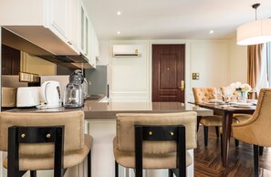 A modern hotel room with a dining area, kitchenette, and a large window.