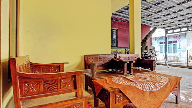 A dining area with wooden furniture and a table covered with a patterned cloth. - Hotel O Juan Kostel (Kembaran)