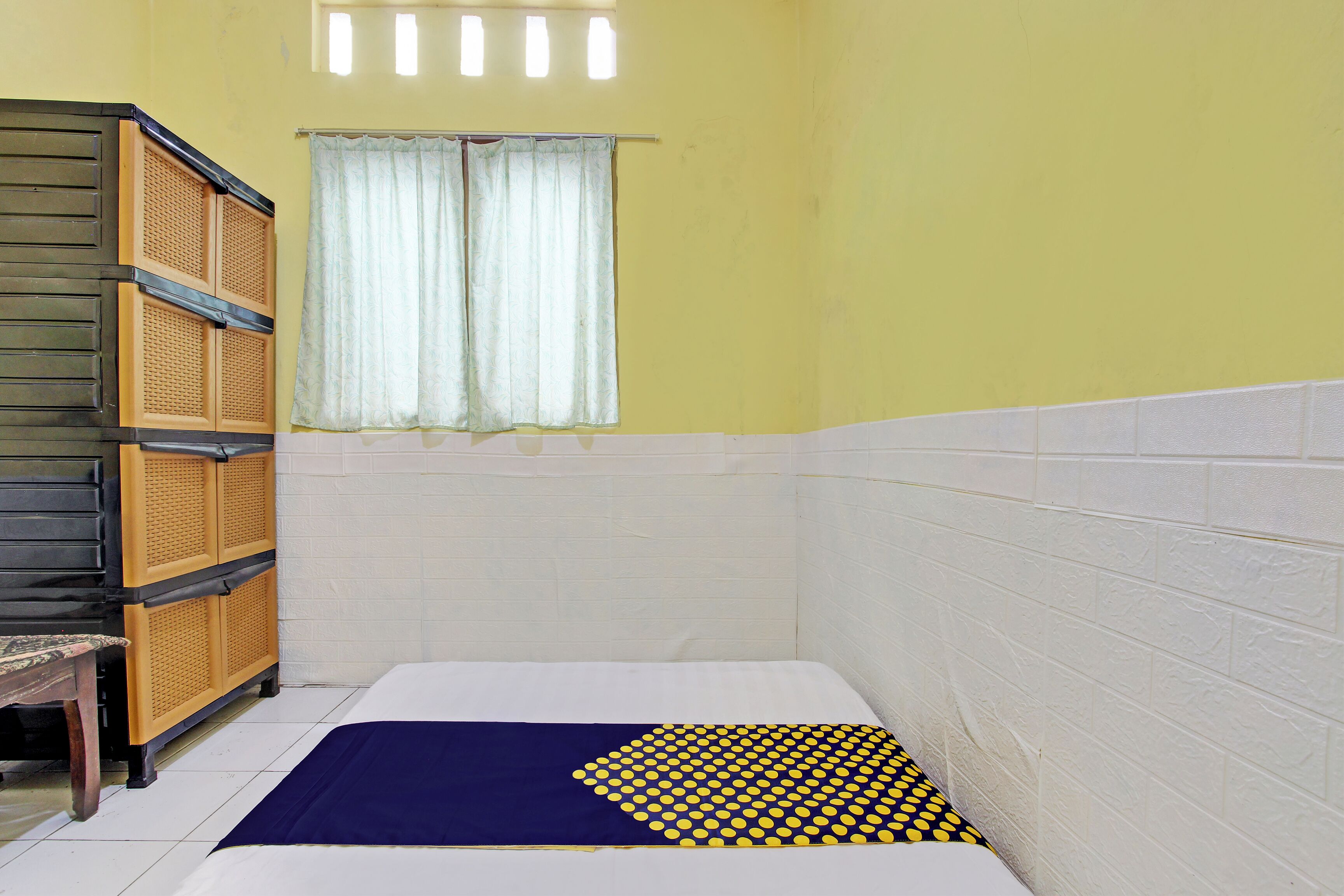 Un baño pequeño y estrecho con una cama individual, un armario de madera y una ventana con cortina.