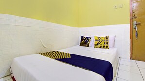 A single bed with a white and blue bedspread, two patterned pillows, and a wooden door to the right. - Hotel O Juan Kostel (Kembaran)