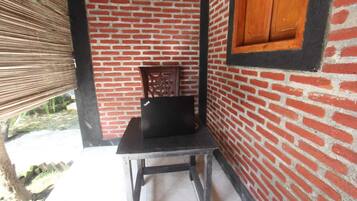 Una habitación con pared de ladrillo, una silla de madera, una mesita y una ventana con contraventanas de madera.