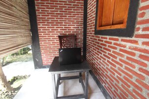 Una habitación con pared de ladrillo, una silla de madera, una mesita y una ventana con contraventanas de madera.