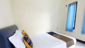 Una cama individual con colcha blanca y azul estampada, un almohadón blanco y un sofá azul con un almohadón blanco.