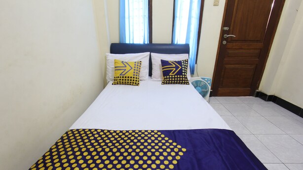 A bed with a blue and yellow polka dot bedspread, two pillows with arrow designs, and a wooden door in the background. - OYO Life 93157 Kos Kaloka (Janapria)