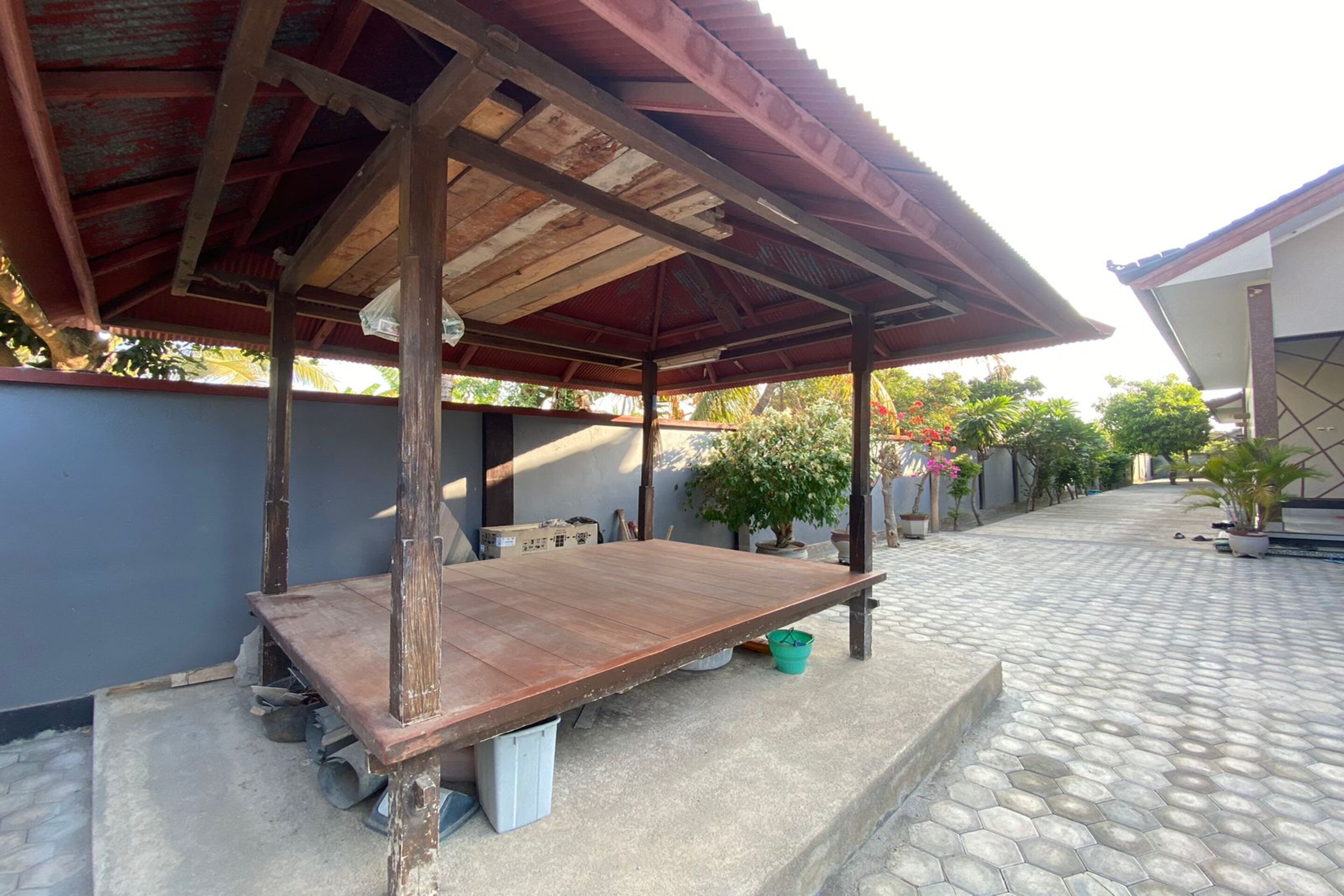 Un espace extérieur abrité, doté d’un banc en bois, d’un sol en béton et de plantes en pot.
