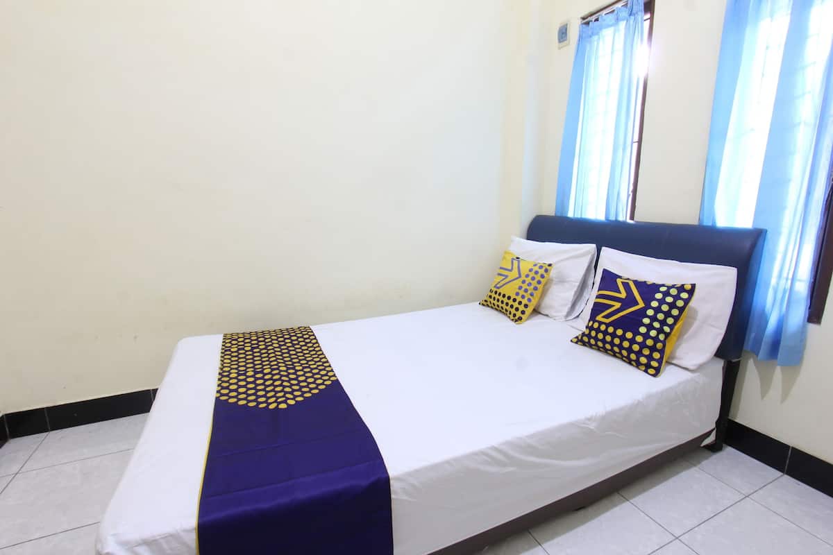 A single bed with a white and blue bedspread, two pillows with geometric patterns, and a window with blue curtains.