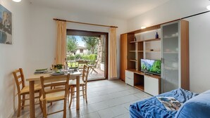 A living room with a dining area, a television, and a bookshelf. - I Fari Apartments 600m From The Beach (Loiri Porto San Paolo)