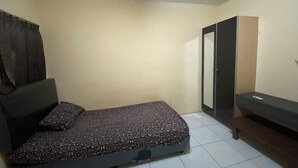 Une petite chambre avec un lit simple, une couvre-lit à motifs sombres, une tête de lit, une armoire et un banc.