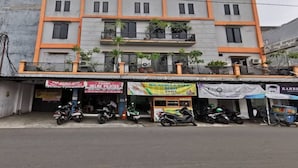 Un immeuble à plusieurs étages, doté de balcons, avec plusieurs boutiques au rez-de-chaussée et des motos garées devant.