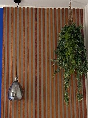 A room with vertical wooden slats on the wall, a hanging plant, and a pendant light. - La Corte del Sole (Vieste)