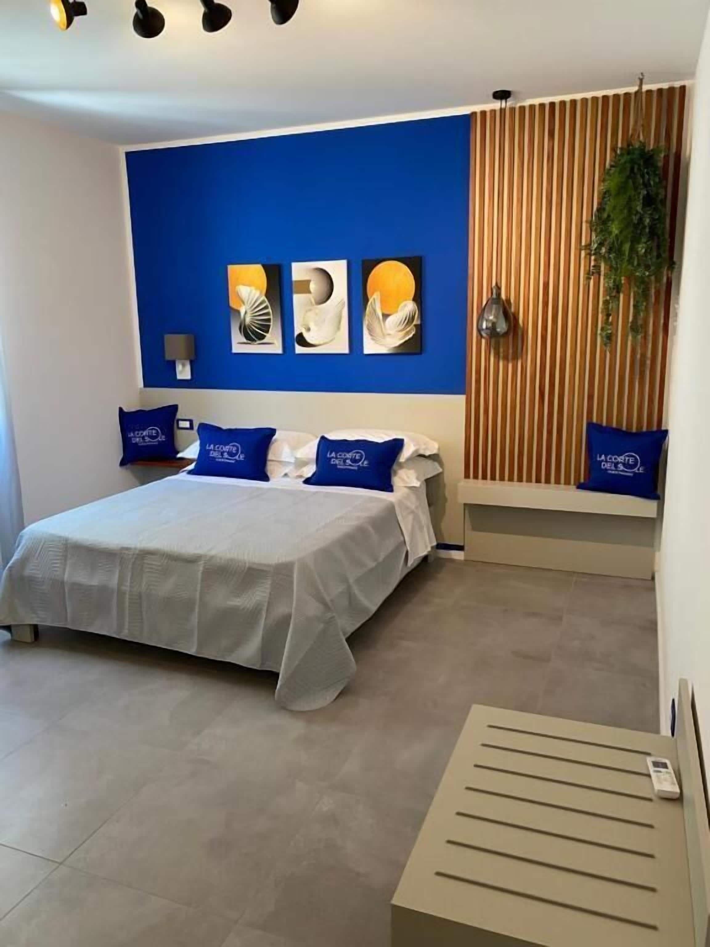 A modern bedroom with a bed, blue pillows, a wall-mounted lamp, and a vertical wooden panel.