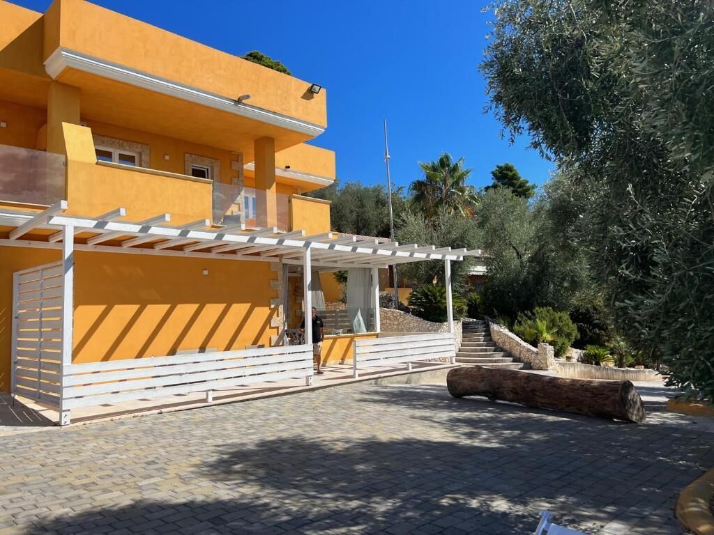 Um edifício amarelo com área externa coberta e escadaria que leva a um nível superior.
