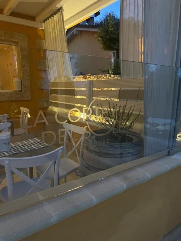 A dining area with a glass table and chairs, a stone wall, and a view of a garden with a potted plant. - La Corte del Sole (Vieste)