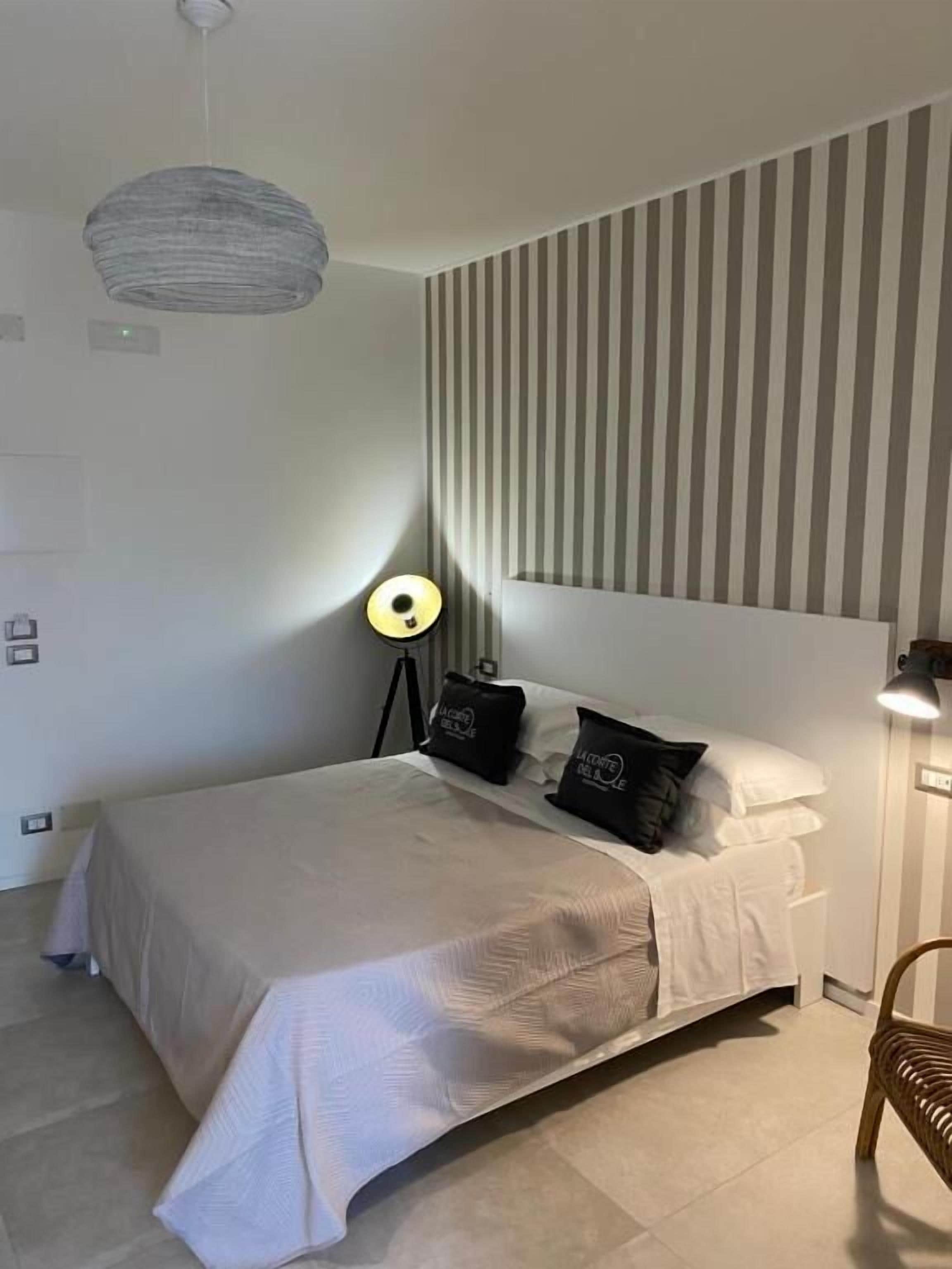 A neatly arranged bedroom with a bed, pillows, a bedside lamp, and a striped wall.