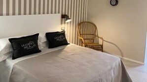 Una camera da letto con un letto grande, carta da parati a righe, un lampadario, una sveglia e una sedia in vimini.