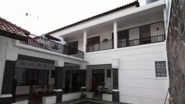 A two-story building with a white exterior, a balcony on the upper floor, and a small courtyard with a lawn and planters. - OYO Life 93158 Kost Asaka (Tangerang)