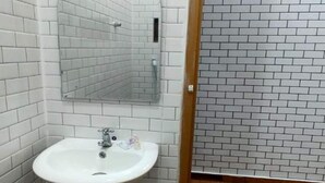 A bathroom with white tiled walls, a wooden door, and a white sink with a mirror above it. - OYO Life 93158 Kost Asaka (Tangerang)