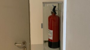 A fire extinguisher mounted on a wall near a door with a handle and lock. - OYO Life 93158 Kost Asaka (Tangerang)