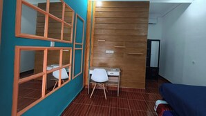 A room with a wooden wall panel, a desk with a chair, a bed, and a window with a wooden frame. - OYO Life 93158 Kost Asaka (Tangerang)